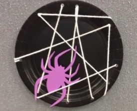 black paper plate with white yarn web and purple spider