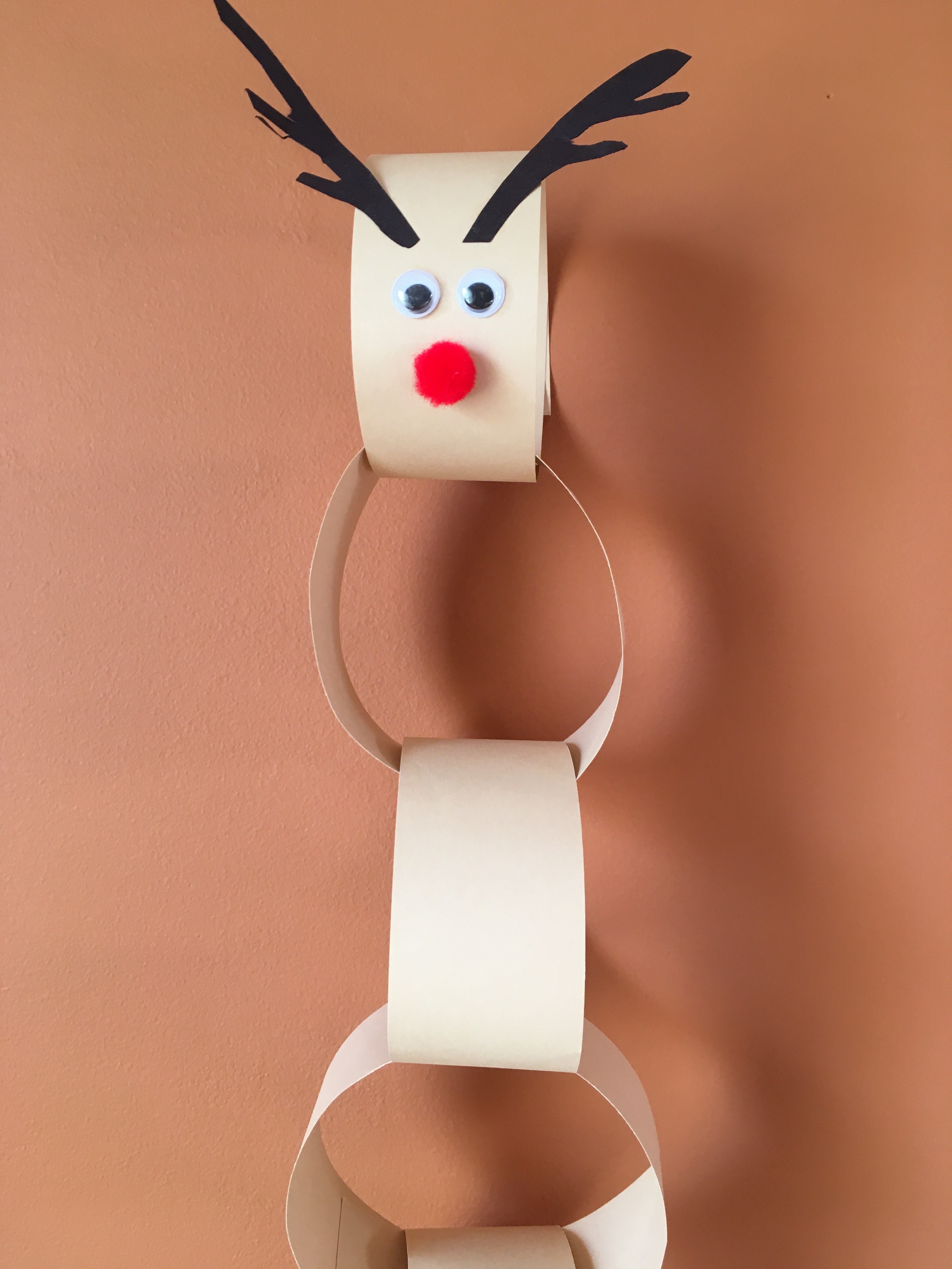 tan paper chain reindeer with brown antlers, wiggle eyes and red pom pom nose