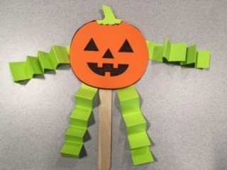 orange jack-o'-lantern stick puppet with green arms and legs