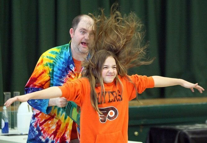A picture of an adult with a child. The child has their hair straight up in the air after volunteering for a science project.