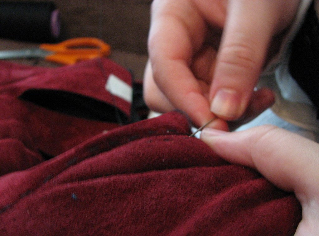 Image of a person hand sewing a dark red fabric.