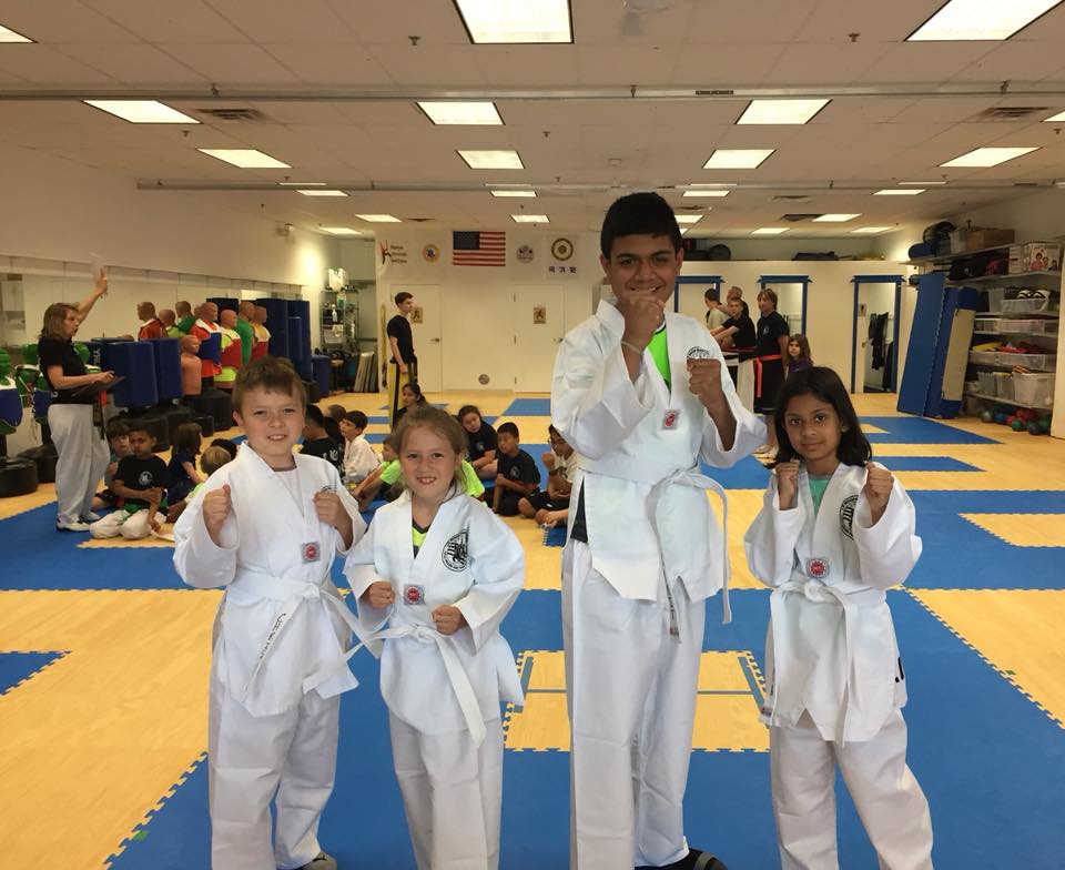 Four kids posing in front of a camera smiling in their martial arts uniform.