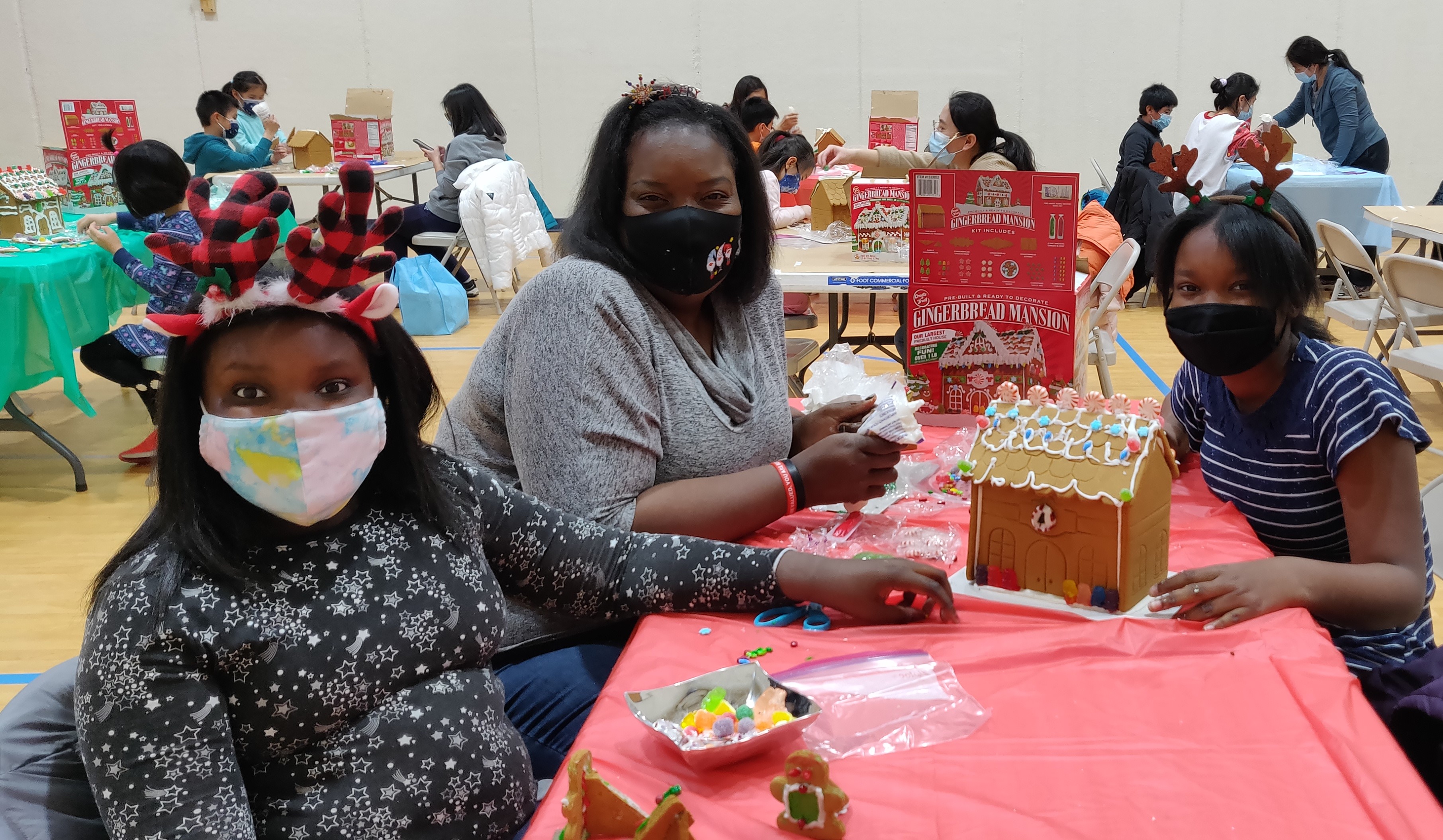 A mother and her two daughters pose with their decorated gingerbread house