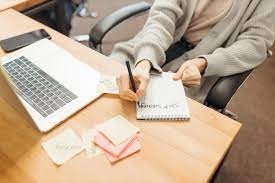 Image of person writing on a notepad near computer.