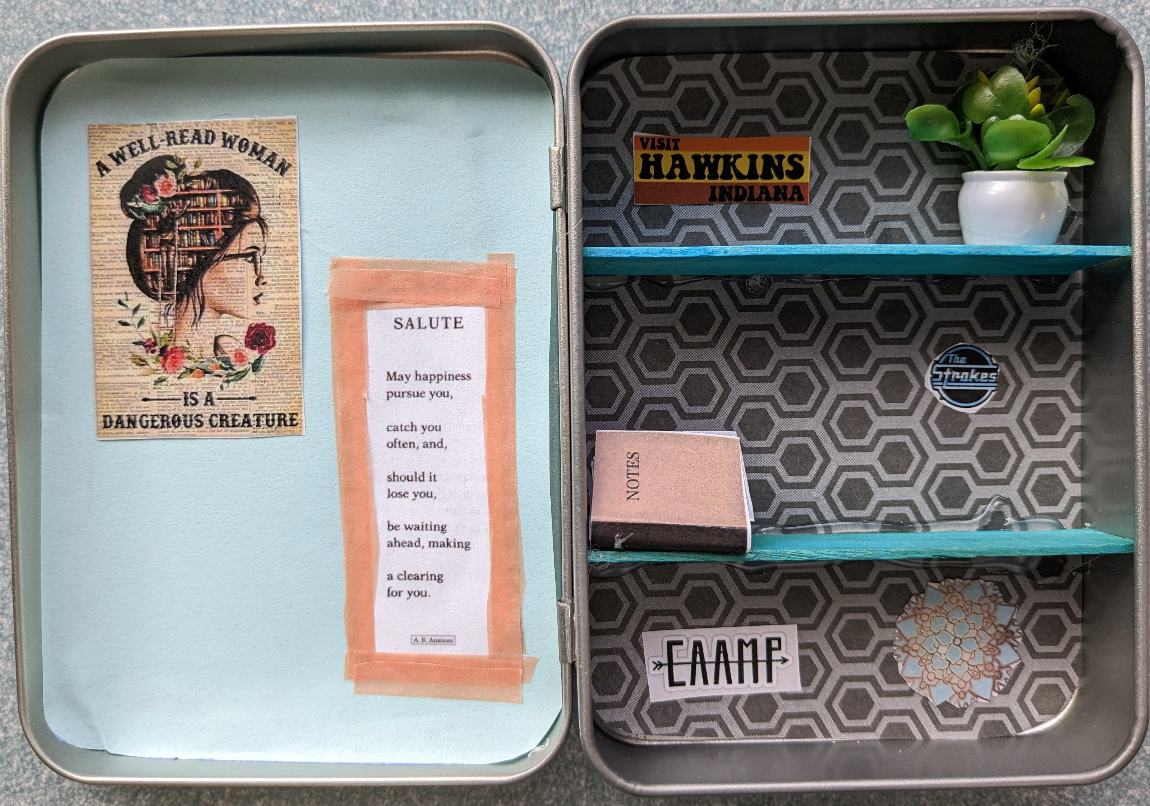 Sample mini bookcase made from a rectangular hinged tin. On the left: light blue paper backround with "a well-read woman is a dangerous creature" poster and a poem, "Salute" by A.R. Ammons. On the right: gray geometric paper backround, two teal shelves made from popsicle sticks. Top shelf: "Visit Hawkins Indiana" sticker and fake potted plant. Middle shelf: mini notebook made from folded paper and The Strokes sticker. Bottom shelf: CAAMP sticker and teal and gold paper mandala.