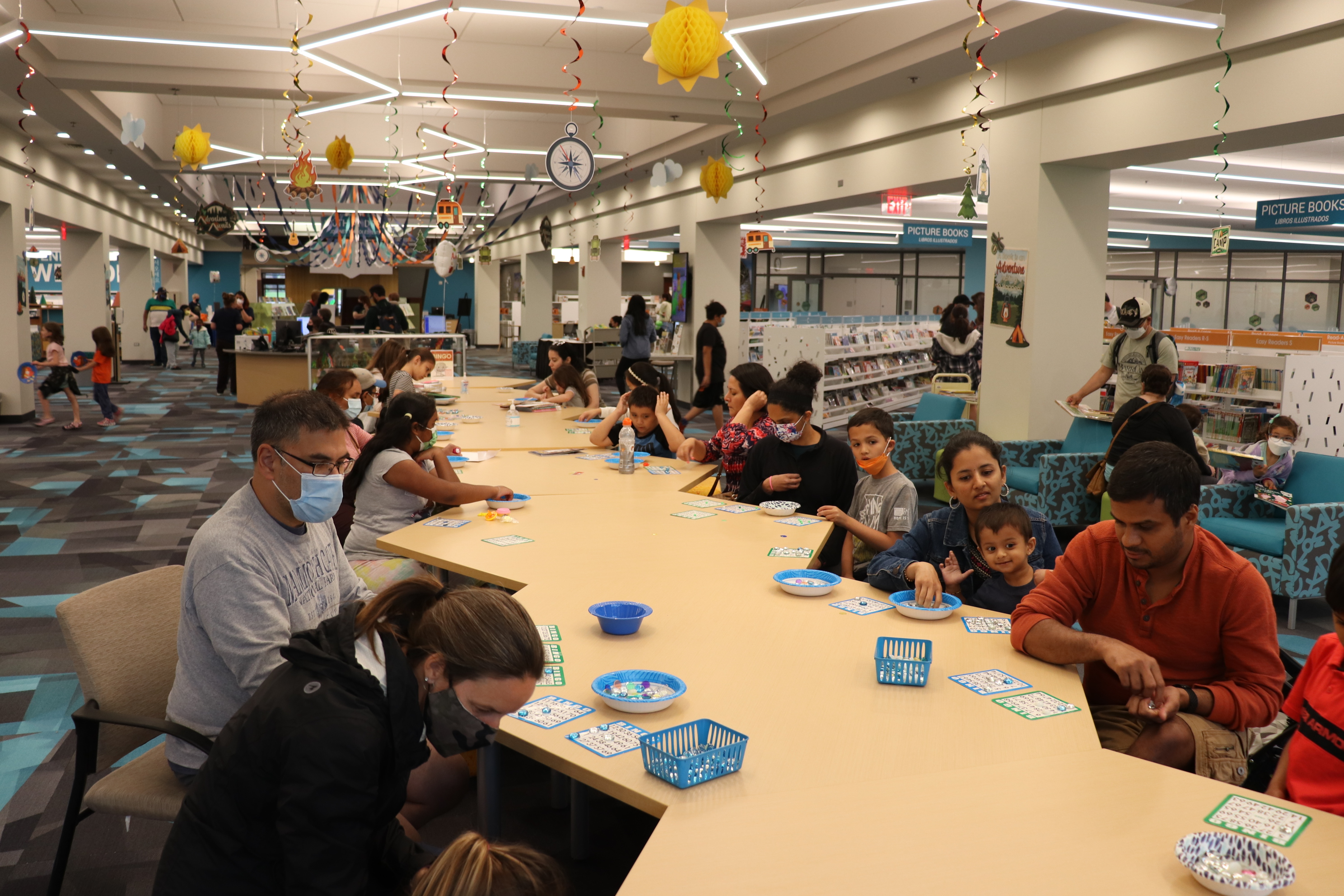 Families playing bingo at the library. The library decorated with streamers from the ceilings.