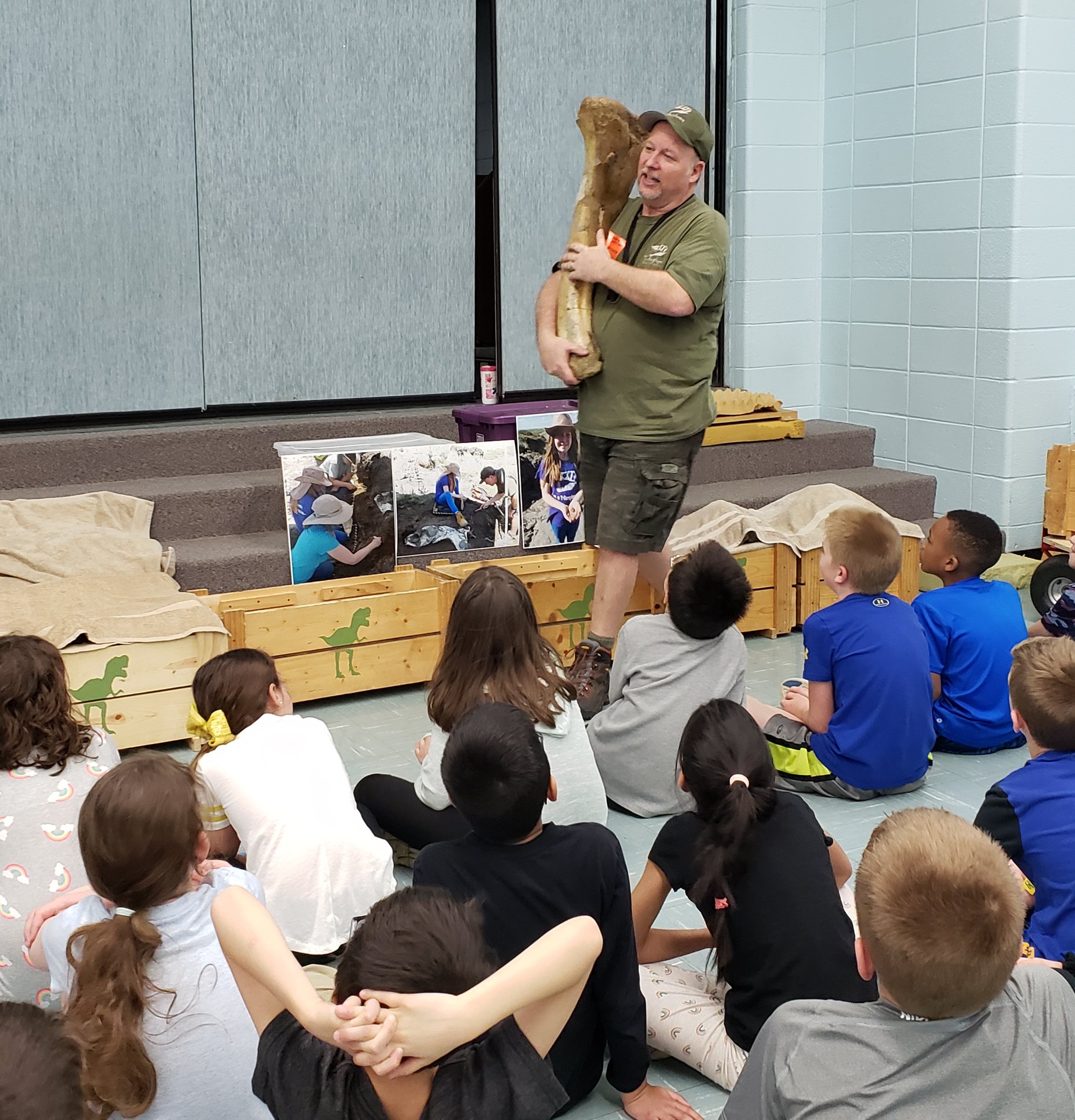Presenter from T-Rexplorers holding a large dinosaur bone in front of a group of kids.