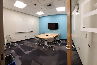 Study Room 1E showing a table with six rolling chair, a white board, and a digital display