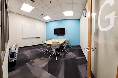 Study Room 1G showing a table with six rolling chair, a white board, and a digital display