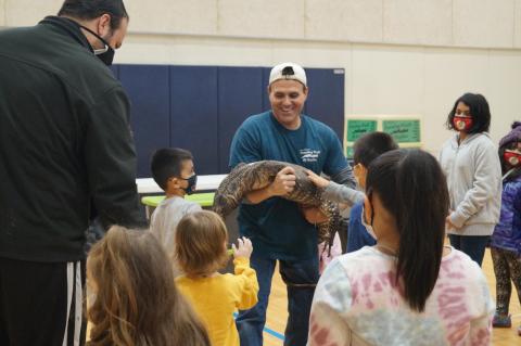 Dave DiNaso holding a large reptile with children petting the reptile