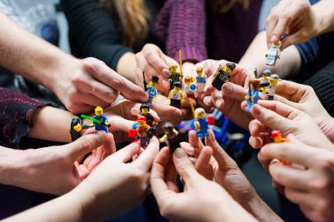 Multiple hands holding LEGO figurines in a circle
