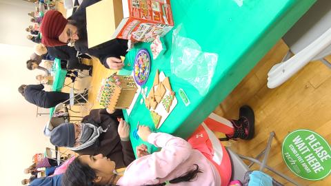 A mother, father, and daughter decorating a gingerbread house with candy and icing.