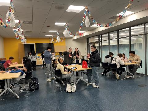 photo of a room full of tables with students sitting and eating snacks.