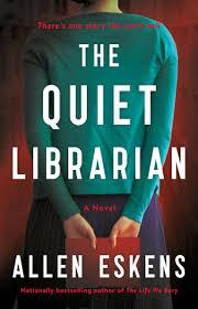A person stands with their back turned against a deep red background. Their hands are clasped behind them holding a red book. Bold white text reads “The Quiet Librarian” with the author’s name, Allen Eskens, at the bottom.